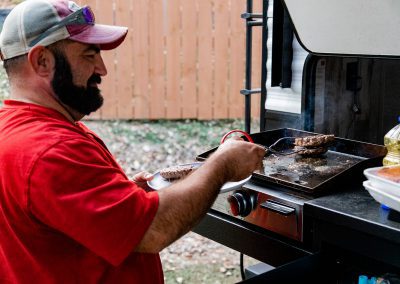 man grilling burgers at campsite
